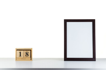 Wooden calendar 18 June with frame for photo on white table and background