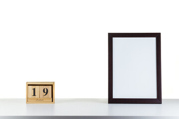 Wooden calendar 19 June with frame for photo on white table and background