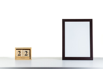 Wooden calendar 22 June with frame for photo on white table and background