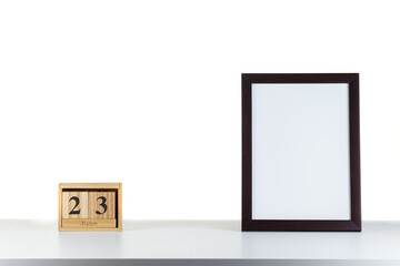 Wooden calendar 23 June with frame for photo on white table and background
