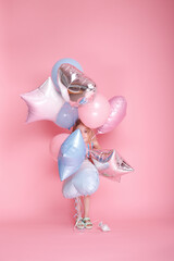bunch of blue with pink balloons in the hands of a girl on a pink studio background