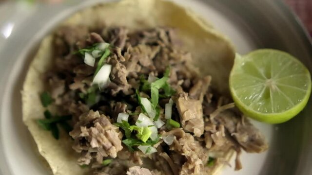 Beef barbacoa taco and sliced lime on white plate