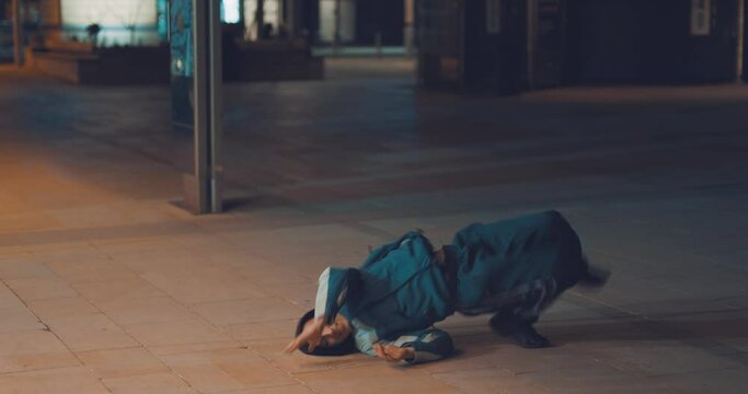 Cool hip young dancer impressive breakdancing moves in city street at night