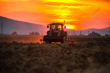 Beautiful sunset, farmer in tractor preparing land with seedbed cultivator © ValentinValkov