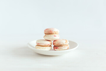 Tasty french macaroons on a white plate. White wooden background.