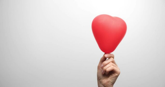 Women's hands with a heart-shaped balloon on a light background