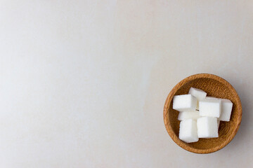 Sugar cubes in a wooden plate on the kitchen table. On right side of the photo. Top view. With copy space