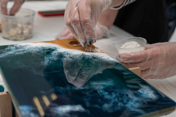 artist hands decorating a wooden serving board with white stones, epoxy resin, selective focus,...