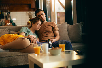 Young couple fell a sleep on the sofa while watching TV at home.