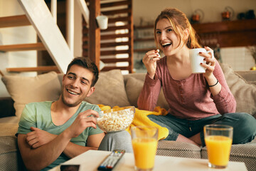 Happy couple eating popcorn while watching movie at home.