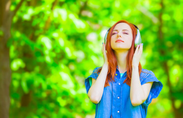 Redhead women with headphones in the park.