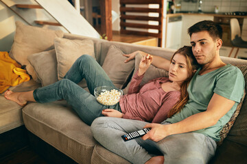 Relaxed couple watching TV and eating popcorn on the sofa at home.