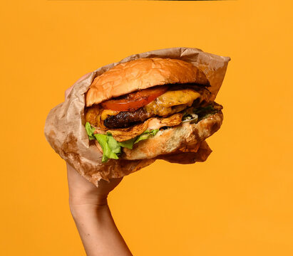 Woman hands hold big cheeseburger barbeque sandwich burger with marble beef cheese tomatoes lettuce on yellow orange background