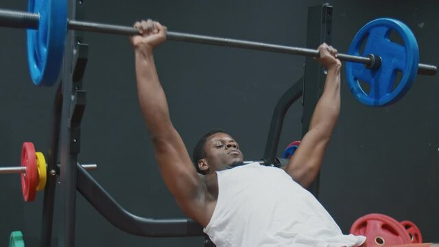 Young muscular afro powerful man does a bench press with a barbell lying on a bench.