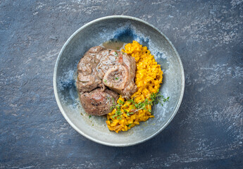 Modern style traditional braised Italian ossobuco alla Milanese with saffron risotto and baby broccoli in white wine meat sauce served as top view on a Nordic design plate with copy space
