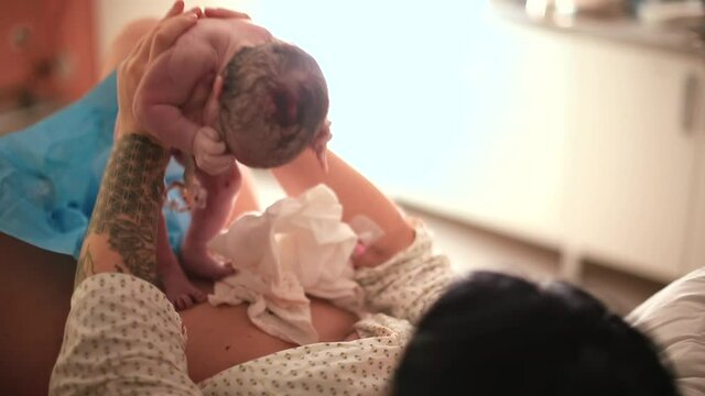 A woman holds a newborn baby in her arms. She puts it on her stomach, the first physical contact, the exchange of bacteria. Natural parenting.
