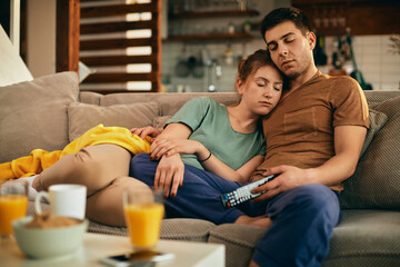 Young couple napping while relaxing on the sofa and watching TV.