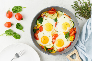 Fried eggs poached with vegetables on teflon pan - pepper, tomatoes, spinach, peppers, onion and garlic. Mediterranean cousine. Keto meal, FODMAP recipe, low carb. Top view