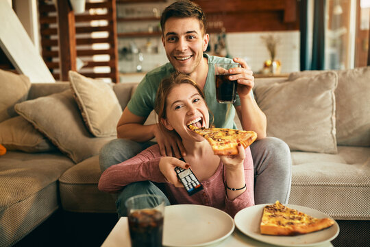 Happy couple eating pizza while watching movie at home.