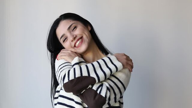 young beautiful woman feeling in love, smiling, cuddling and hugging self, staying single, being selfish and egocentric against grey wall