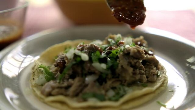 Adding red hot sauce to a beef barbacoa taco