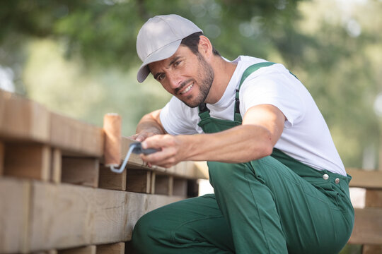 happy man painting wooden fence in the garden sitting