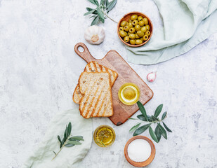 Fototapeta na wymiar Top view olive oil, olives, toast bread and leaves on white background, space for text