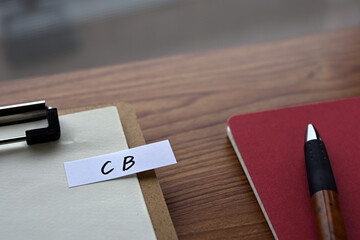 On the desk there is a clipboard, a notebook, and a stickynote with the word CB written on it. It...