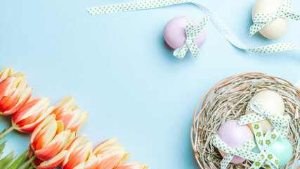Easter gold. Colorful egg with tape ribbon, spring tulips, feathers on pastel blue background in Happy Easter decoration. Traditional design in top view.
