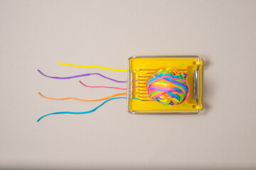 Yellow egg slicer with multicolored rubber bands on a gray background