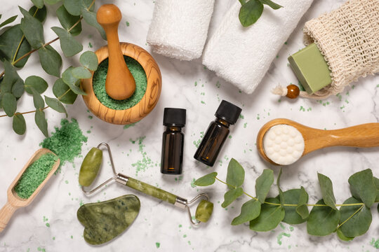 Natural skin care and aromatherapy with eucalyptus essential oil bottles, bath salt, beauty jade roller, gua sha on marble background. Spa, wellness, massage and relaxation concept. Top view, flat lay