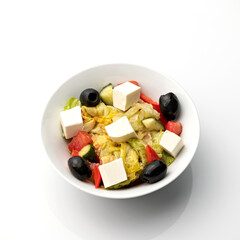 Bowl of Greek salad with feta cheese and olives. Food plate isolated on white background. Vegan or vegetarian cuisine. Top view. Appetizer dish from restaraunt menu. Exquisite served dish.