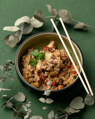 Asian lunch. Bowl of stew with sesame seeds and chinese chopsticks on green background. Top view. Traditional Oriental vegetable dish. Vegetarian or vegan cuisine. Vertical format, 4x5. 