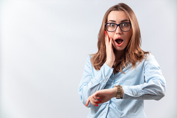 beautiful girl in a blue shirt and glasses looks at the clock on a white background. isolated