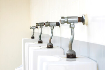 Rusty urinal faucets around an old urinal in the bathroom at the gas station. Dirty and unhygienic rust stains, space for text,Blurred background, Focus on the faucet