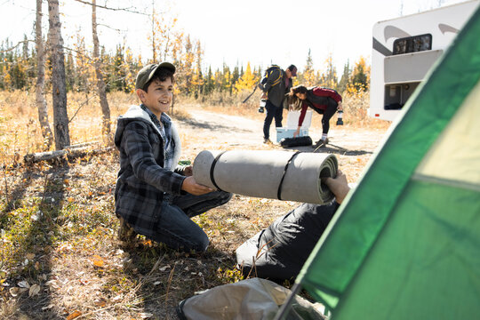 Boy Putting Camping Equipment Into Tent Next To RV