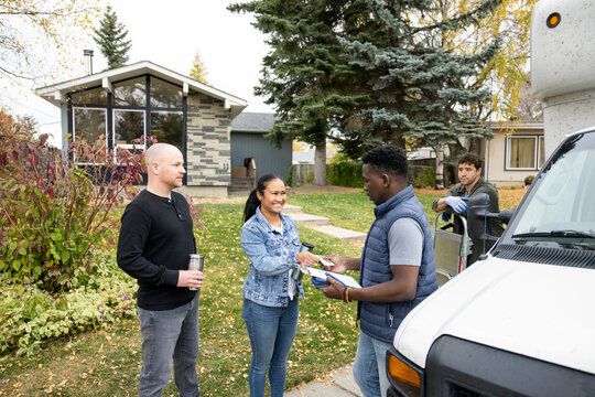 Couple Paying Movers At Moving Van Outside New Home