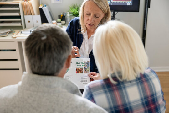 Doctor showing nutrition brochure to senior couple in clinic exam room
