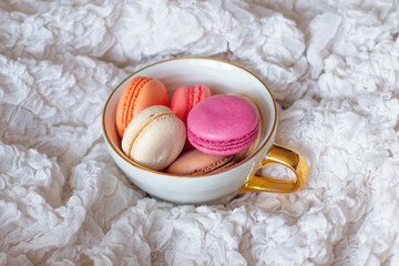 Sweet dessert, vanilla macaroons in mug on white blanket in bed. Romantic morning breakfast.