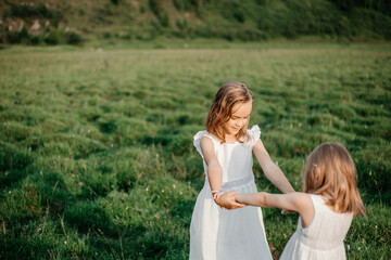 Happy children in white dresses play on the grass in summer. Portrait of two sisters. Children's friendship