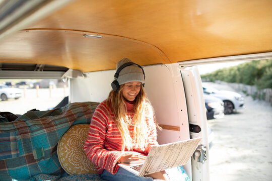 Happy young woman using headphones and laptop in sunny camper van