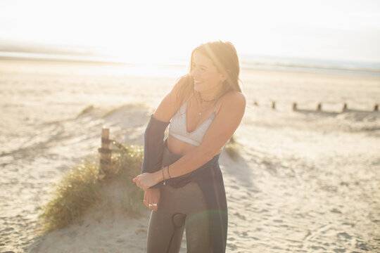Young female surfer removing wet suit on sunny beach