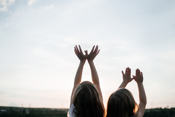 Two little girls fun playing in summer outside. Girls hands up ts to the sky and make bird figures. Children's friendship and a happy childhood