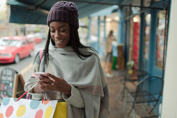 Young woman with shopping bag using smart phone on sidewalk
