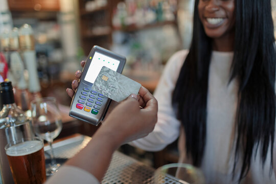 Close up customer paying female bartender with smart card in pub