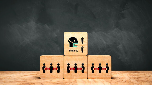 stack of cubes with social distancing, face mask and syringe symbols and the text COVID-19 in front of a blackboard - Powered by Adobe