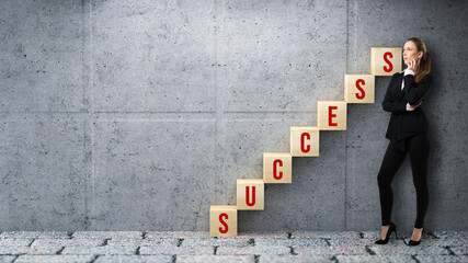 Success in business or corporate ambition concept with a stylish female businesswoman standing alongside a staircase of wooden cubes spelling Success against a grey wall and copyspace
