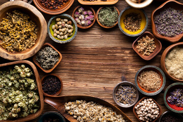 Natural medicine background. Assorted dry herbs in bowls and brass mortar on rustic wooden table.
