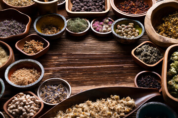 Natural medicine background. Assorted dry herbs in bowls and brass mortar on rustic wooden table.