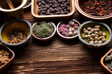 Natural medicine background. Assorted dry herbs in bowls and brass mortar on rustic wooden table.